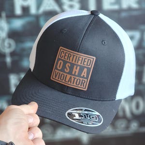 May include: A black and white trucker hat with a brown leather patch that says "CERTIFIED OSHA VIOLATOR".
