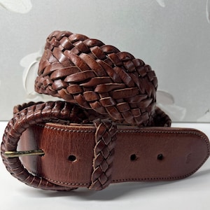 K&ouml;nnte beinhalten: Ein dunkelbrauner Lederg&uuml;rtel mit einem breiten geflochtenen Riemendesign. Der G&uuml;rtel verf&uuml;gt &uuml;ber eine passende, mit geflochtenem Leder bezogene ovale Schnalle und eine einzelne geflochtene Lederschlaufe. Das Ende hat drei L&ouml;cher zur Anpassung.