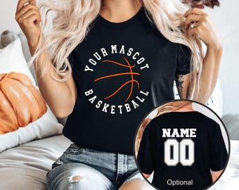 Może przedstawiać: Czarny t-shirt z białą okrągłą grafiką z napisem YOUR MASCOT BASKETBALL i pomarańczowym konturem piłki do koszykówki. Wstawione koło pokazuje tył koszulki z białym napisem NAME i numerem 00 nadrukowanym w kolorze białym.
