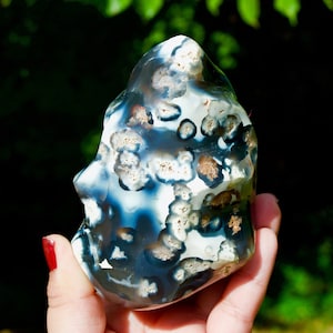 May include: A polished agate stone featuring a deep blue and white color palette with distinct circular inclusions. The surface displays a smooth, glossy texture with varied patterns of dark blue, translucent white, and small, textured beige spots.