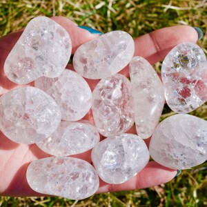 May include: A collection of tumbled clear quartz crystals with a cloudy, milky appearance. The crystals are smooth and polished, with a variety of shapes and sizes.