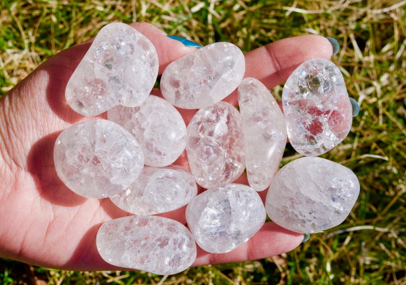 May include: A collection of tumbled clear quartz crystals with a cloudy, milky appearance. The crystals are smooth and polished, with a variety of shapes and sizes.