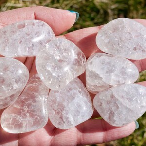 May include: A collection of seven clear quartz crystal tumbled stones. The stones are smooth and have a cloudy, milky appearance.