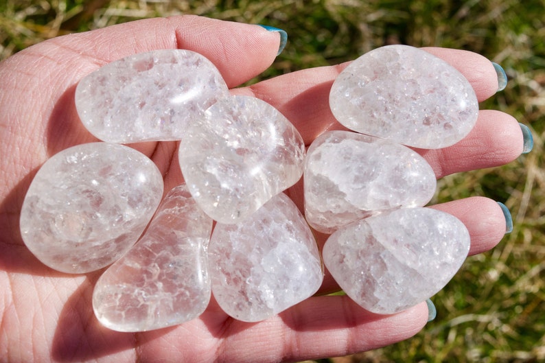 May include: A collection of seven clear quartz crystal tumbled stones. The stones are smooth and have a cloudy, milky appearance.