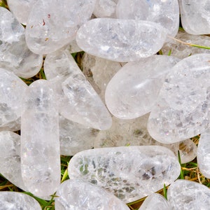 May include: A collection of clear quartz tumbled stones, each with a unique, naturally occurring pattern of inclusions. The stones are smooth and polished, with a slightly milky white hue.