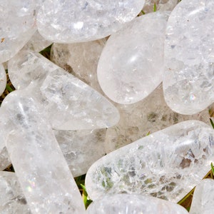 May include: A collection of clear quartz crystal stones, each with a unique shape and texture. The stones are smooth and polished, with a slight iridescent sheen.