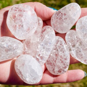 May include: A collection of eight clear quartz crystal tumbled stones with a cloudy, milky appearance. The stones are smooth and polished, with a variety of sizes and shapes.
