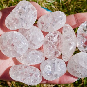 May include: A collection of ten clear quartz tumbled stones with a cloudy, milky appearance. The stones are smooth and polished, with a variety of sizes and shapes.