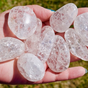 May include: A collection of clear, tumbled quartz crystals with a cloudy, frosted appearance. The crystals are smooth and polished, with a natural, irregular shape.