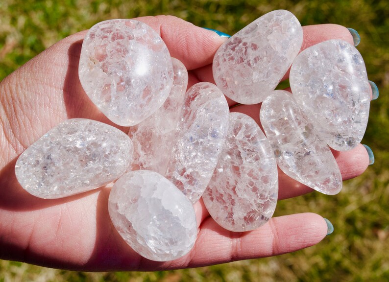 May include: A collection of clear, tumbled quartz crystals with a cloudy, frosted appearance. The crystals are smooth and polished, with a natural, irregular shape.