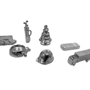 May include: A set of silver-colored game pieces for a board game. The pieces include a dog bowl, a golf club, a Christmas tree, a construction helmet, a cell phone, and a delivery truck.