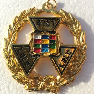 May include: A gold-colored pendant with a wreath design. The center features a triangular design with the words "LIBERTY" and "A.D. 1776" on two of the points. The top point has a small square with the word "FREEDOM" in Thai script.