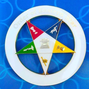 May include: A white, circular, metal pin with a gold border and the words "Order of Eastern Star" around the edge. The centre of the pin features a five-pointed star with five different coloured triangles, each with a symbol in the centre.