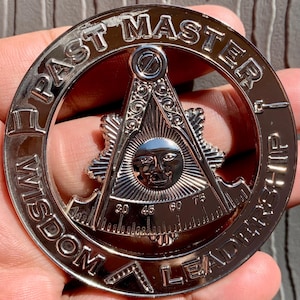 Może przedstawiać: Srebrna metalowa odznaka masońska Past Master z kompasem i kwadratem. Odznaka zawiera napisy "Past Master", "Wisdom" i "Leadership" wokół obwodu. Środek odznaki przedstawia słońce z twarzą i kompas oraz kwadrat.