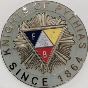 May include: A silver and white circular pin with the text "Knights of Pythias Since 1864". The center of the pin features a silver triangle with a blue, white, and red section. Each section has a letter, "F", "C", and "B" respectively.