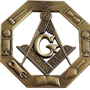 Puede incluir: Un emblema masónico de color bronce. El diseño octogonal presenta una escuadra y un compás con una "G" central. Incluye símbolos como un ojo, un mazo, un reloj de arena y un libro abierto.