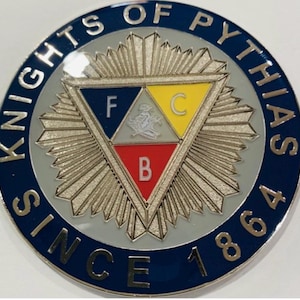 May include: A circular emblem with a blue border, featuring the text "KNIGHTS OF PYTHIAS" and "SINCE 1864". The center has a triangle divided into three sections: blue with "F", yellow with "C", and red with "B". A silver sunburst design surrounds the triangle.
