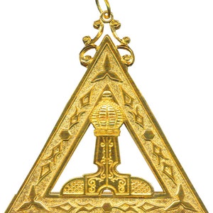 May include: A gold-colored Masonic pendant in the shape of a triangle with an ornate design. The pendant features a stylized depiction of a builder's hammer and a compass.
