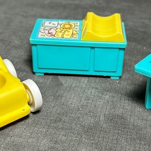 May include: A set of three vintage plastic toys for a baby doll or action figure. The set includes a yellow stroller with white wheels, a blue changing table with a yellow changing pad, and a blue high chair.