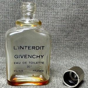 May include: A clear glass bottle of L'Interdit perfume by Givenchy. The bottle has a black label with the text "L'Interdit Givenchy Eau de Toilette 90&deg; Paris France". The bottle has a silver cap.
