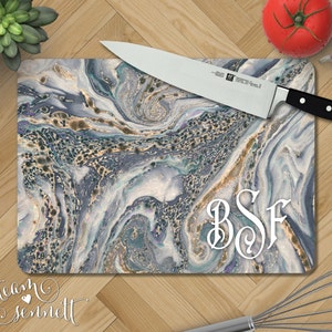 May include: A blue and gold marble-patterned cutting board with the monogram "BSF" in white. The board is made of tempered glass and is perfect for serving and displaying food.
