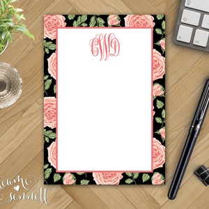 May include: A black and white notepad with a pink floral border. The notepad has a white writing area and a pink monogram in the top center. The monogram is "CWD".
