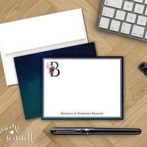 May include: A white card with a navy blue border and a floral monogram of the letter "B" in the top left corner. The card has a white border and the text "KENDALL & HARRISON BRADLEY" at the bottom.