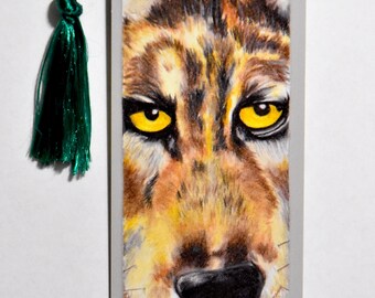 Puede incluir: Un primer plano de un marcapáginas de lobo con un borla verde. El pelaje del lobo es marrón y amarillo, y sus ojos son de un amarillo brillante. El marcapáginas está hecho de cartulina y mide aproximadamente 15 cm de alto.