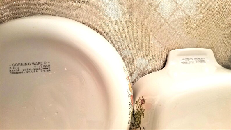 May include: Two white Corning Ware baking dishes with a floral pattern. The larger dish is 9 1/2 inches and is marked "Range, Oven, Microwave, Corning, NY, USA, 378 MA".