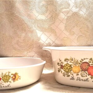 May include: Two white oval baking dishes with a floral design featuring green leaves, red tomatoes, and yellow lemons. The dishes have the text "Le Persil Le Sauge" on the bottom.