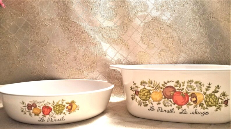 May include: Two white oval baking dishes with a floral design featuring green leaves, red tomatoes, and yellow lemons. The dishes have the text "Le Persil Le Sauge" on the bottom.