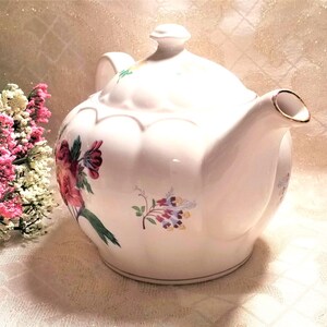May include: A white teapot with a floral design. The teapot has a scalloped edge and a gold trim. The flowers are pink, red, blue, and yellow.