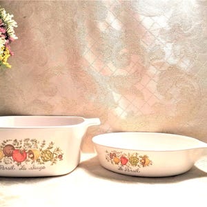 May include: Two white ceramic casserole dishes with floral designs and the text "Le Peril" and "La Sauge".