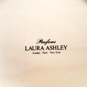 May include: A white ceramic plate with the text "Parfums LAURA ASHLEY London &middot; Paris &middot; New York" printed in black.