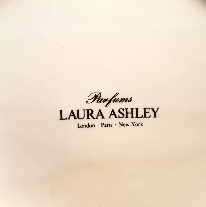 May include: A white ceramic plate with the text "Parfums LAURA ASHLEY London &middot; Paris &middot; New York" printed in black.