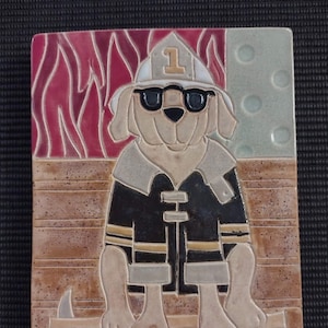 May include: A ceramic tile featuring a cartoon dog dressed as a firefighter. The dog is wearing a black and yellow firefighter jacket, a red helmet with the number "1" on it, and sunglasses. The dog is sitting on a brown wooden surface with an axe behind it. The background is a red and white flame pattern.