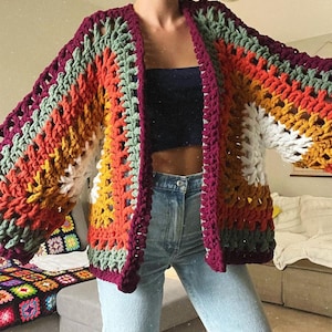 May include: A multi-colored crochet cardigan with a loose fit and open front. The cardigan features stripes of burgundy, orange, yellow, white, and green.