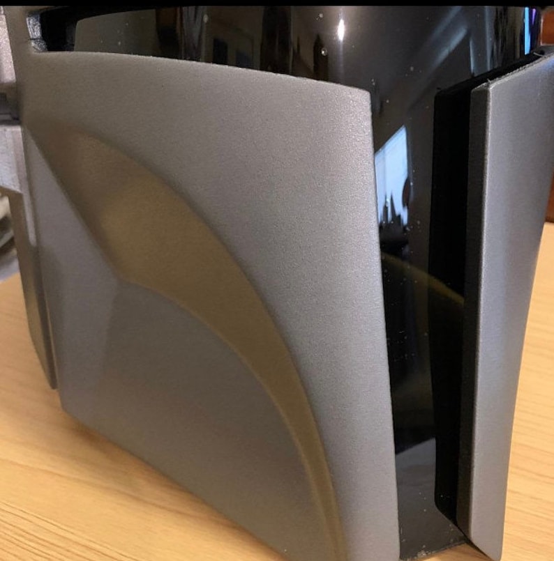 May include: A close-up of a gray and black helmet with a curved, textured surface. The helmet has a black visor and a black strap.