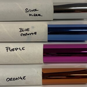 May include: Four rolls of metallic vinyl wrap in different colors: silver, blue chrome, purple, and orange. The rolls are labeled with the color names.