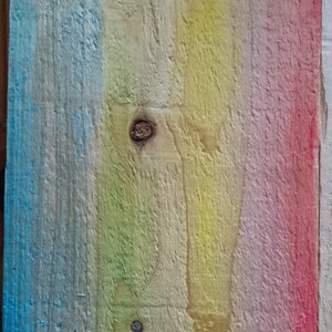 May include: A wooden plank painted in a rainbow gradient of blue, green, yellow, pink, and red. The wood has a natural grain and knots.