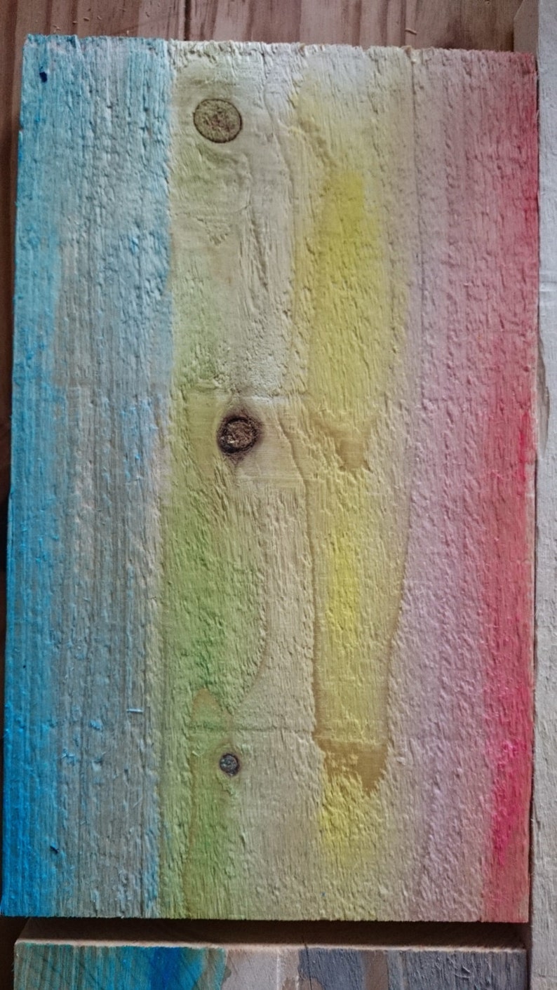 May include: A wooden plank painted in a rainbow gradient of blue, green, yellow, pink, and red. The wood has a natural grain and knots.