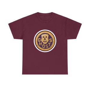 May include: Burgundy t-shirt featuring a circular graphic with a skull and the word "GHOST" in a distressed, vintage style. The graphic is in gold, purple, and white, with a worn appearance. The shirt is a solid burgundy color.