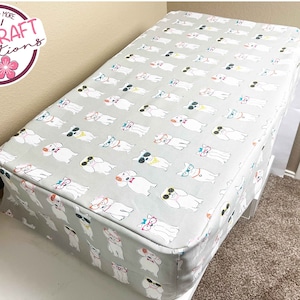 May include: A gray and white fabric cover with a repeating pattern of dogs wearing sunglasses. The cover is for a sewing machine table. The cover has a white border around the edge. The cover is made by A&J Craft Creations.