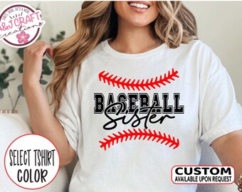 May include: White t-shirt with a red and white baseball stitch design and the text "BASEBALL Sister" in black.