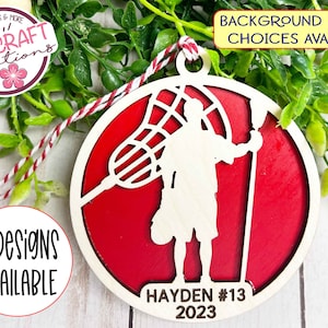 May include: A red and white wooden lacrosse player ornament with the text "HAYDEN #13 2023".