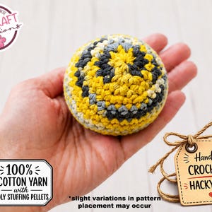 May include: A handmade crocheted hacky sack in yellow, gray, and black, held in a hand. The ball is made with 100% cotton yarn and poly stuffing pellets. A tag reads "Handmade Crocheted Hacky Sack."