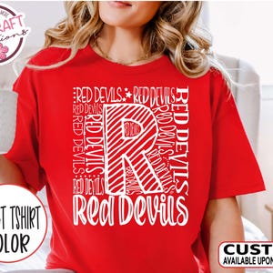 May include: Red t-shirt with a white graphic design featuring the letter "R" made up of the words "Red Devils" repeated multiple times. The words "Red Devils" are also written below the letter "R".