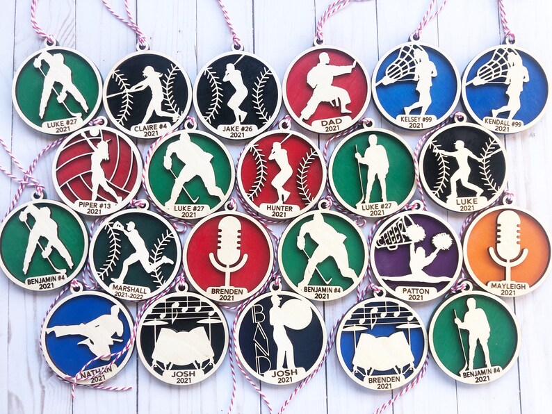 May include: A collection of 18 wooden ornaments featuring various sports and activities. Each ornament is painted in different colors and includes a name and year. The ornaments are perfect for decorating a Christmas tree or adding a personal touch to any space.