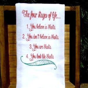 May include: White kitchen towel with red embroidered text that reads "The four stages of life... 1. You believe in Santa 2. You don't believe in Santa 3. You are Santa 4. You look like Santa".