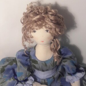 May include: A handmade doll with curly blonde hair, wearing a blue and green floral dress with a blue ribbon.